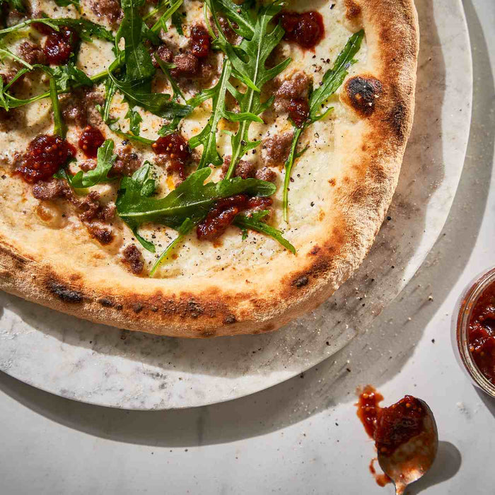 Pizza à la saucisse, chutney à la rhubarbe et roquette, sur un plat placé à côté d'un petit bol de chutney à la rhubarbe