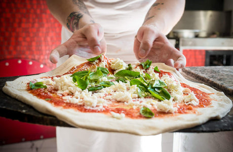 a pair of hands preparing a margherita pizza