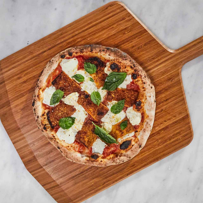 Pizza with fried eggplant, cheese, tomato sauce and basil on a bamboo serving board