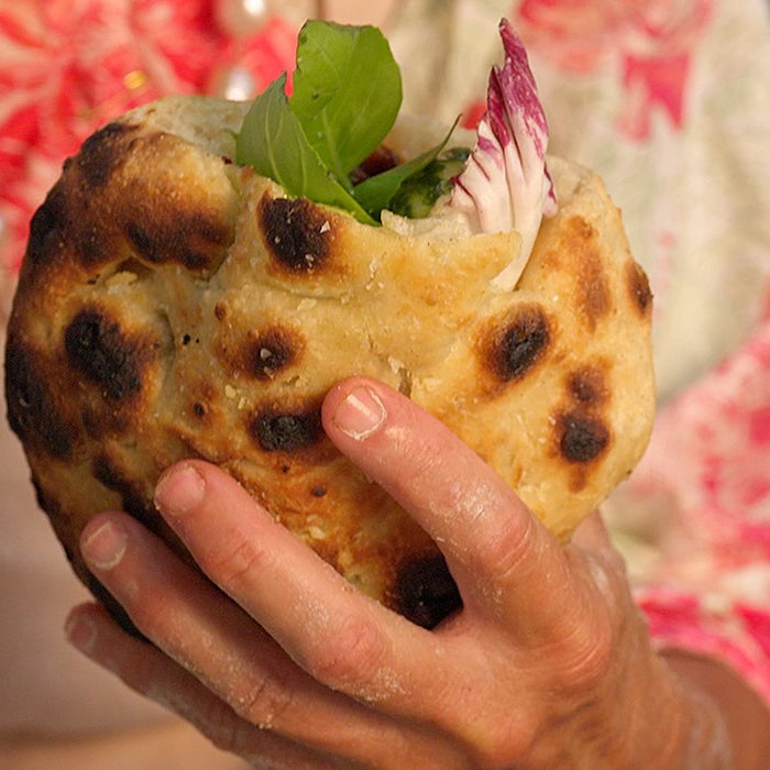 Main tenant une pizzette cuite farcie de petits poivrons, de mozzarella, de radicchio et de basilic.