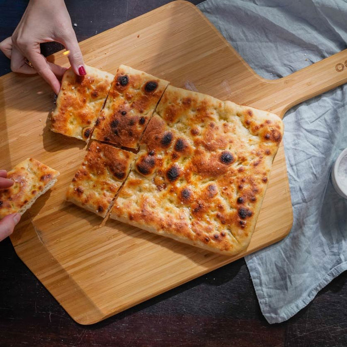 Deux mains tenant des morceaux de pizza romaine sur une pelle à pizza en bambou Ooni.